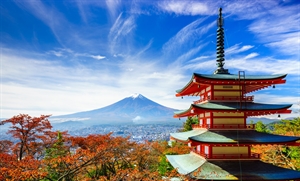Fall view of Japan under a blue sky with red trees and a pagoda in the foreground and Mount Fuji in the background.
