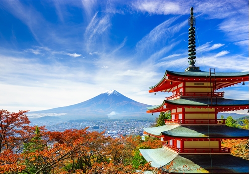 Fall view of Japan under a blue sky with red trees and a pagoda in the foreground and Mount Fuji in the background.